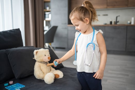 Little girl playing doctor with toys and teddy bear on the sofa in living room at home photo