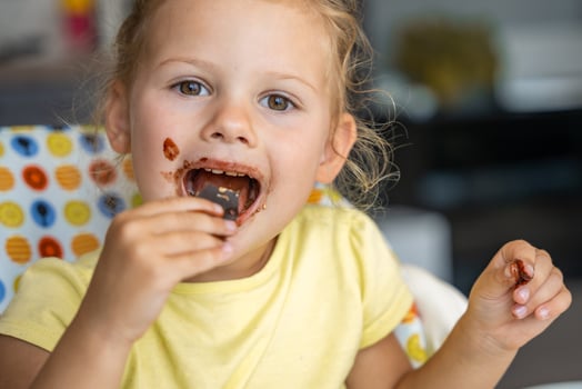 Little girl with blond hair eating homemade chocolate with dirty mouth and hands in home kitchen photo