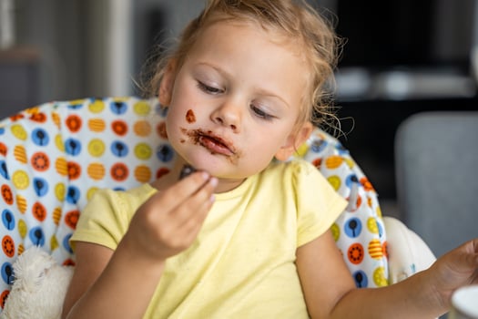 Little girl with blond hair eating homemade chocolate with dirty mouth and hands in home kitchen photo