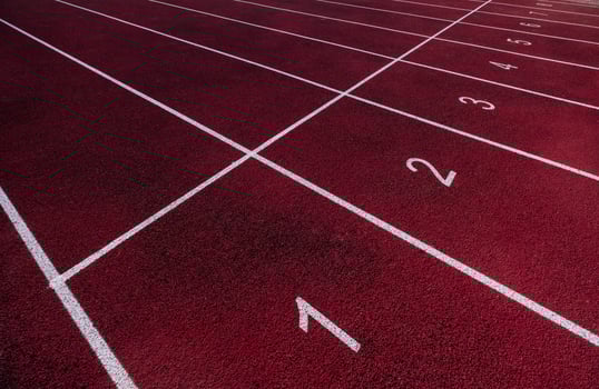 Perspective view of a red running track with white lane numbers and markings, ready for a race photo