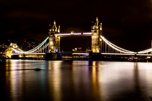 Illuminated suspension bridge over river at night with reflections on water. photo