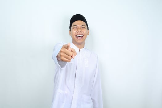 laughing asian muslim man pointing at camera isolated on white background photo