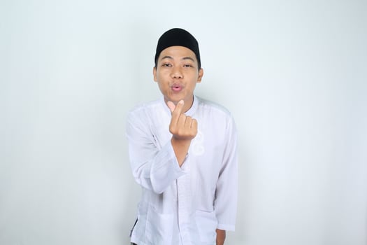 happy asian man muslim blowing kiss with finger shaped korean love sign to camera isolated on white background photo