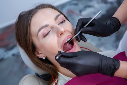Closeup of female patient showing her beautiful white teeth while having treatment at dental clinic, dentist hands in rubber gloves holding dental tools photo