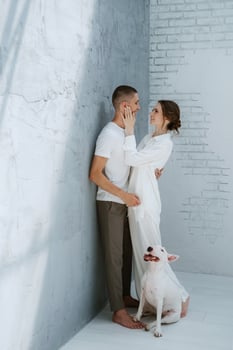 young couple guy and girl in a bright room playing with pet photo