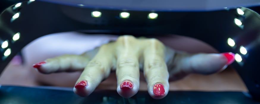 Close up photo of young woman's hand getting a manicure applying semi-permanent nail polish with an ultraviolet lamp.