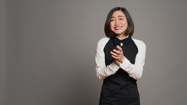Asian server applauding someone and cheering for success, saying congratulations in front of camera. Waitress in formal uniform clapping hands, doing standing ovation gesture. Camera A. photo