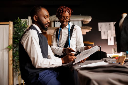 Brainstorming apprentice tailors looking over sketch drawings of bespoke collection imagined by master fashion designer. Teamworking atelier shop colleagues discussing sartorial adjustments to be made photo