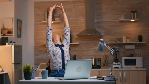 Tired woman working from home streatching after typing on laptop late at night. Busy focused employee using modern technology network wireless doing overtime for job reading writing, searching photo