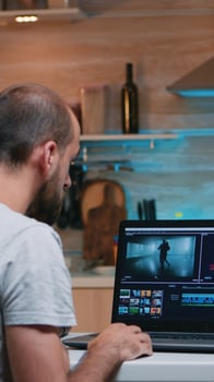 Freelancer editing a video using post production software working from home overtime sitting in the kitchen. Videographer processing audio film montage on professional laptop late at night photo