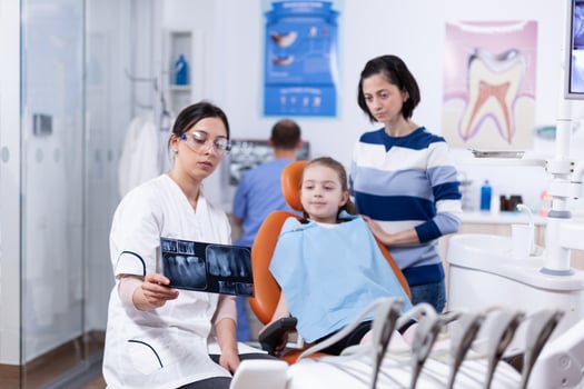 Parent and kid in dentistiry office looking at dental radiography holded by dentist. Stomatologist explaining teeth diagnosis to mother of child in health clinic holding x-ray. photo