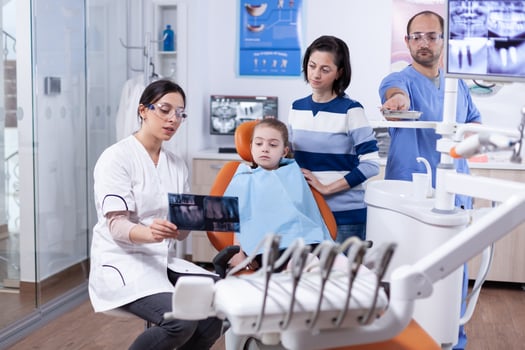 Dentist talking about tooth procedure holds radiography talking with little kid. Stomatologist explaining teeth diagnosis to mother of child in health clinic holding x-ray. photo