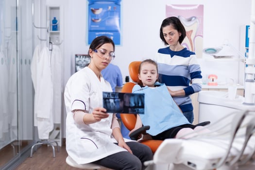 Little girl and parent listening dentist advice pointing at dental radiography. Stomatologist explaining teeth diagnosis to mother of child in health clinic holding x-ray. photo