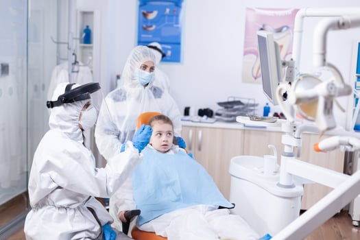 Dentist doctor in the course little kid consultation in dentistery office. Stomatolog in protectie suit for coroanvirus as safety precaution holding child teeth x-ray during consultation. photo