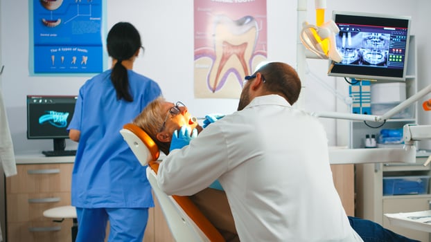 Dentist doctor working in dental unit with nurse and senior patient. Orthodontist speaking to woman sitting on stomatological chair while nurse preparing tools for examination in modern clinic photo