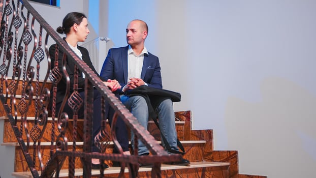 Overworked businesspeople discussing sitting on stairs in corporate business office taking a break. Colleague entrepreneur doing overtime together late at night making plans for deadline project photo