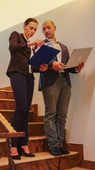 Corporate executive manager holding laptop talking with businesswoman on staircase of business building. Professional successful entrepreneur in team working overtime in modern office photo