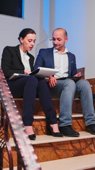 Overworked businesswoman being furious reading raport of deadline financial crisis with coworker. Tired angry colleagues entrepreneur working late together at corporate job sitting on staircase. photo
