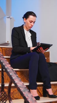 Stressed businesswoman under pressure to finish job deadline doing overtime at night using tablet. Serious entrepreneur working on job project sitting on staircase of business building late at night. photo