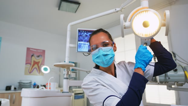 Patient pov in dental chair making performing periodic teeth check in modern stomatological clinic. Dentistry doctor lighting the lamp and examining person wearing protection mask and glasses. photo