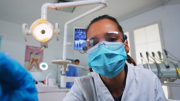 POV of patient in a dental clinic sitting on surgery chair checking affected mass. Dentistry team working in orthodontic office, lighting the lamp and examining person, close-up face in medical mask. photo
