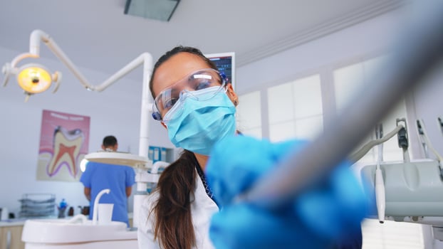 Patient pov to doctor in stomatological office treating teeth of woman. Orthodontic specialist and man assistant working wearing masks and gloves in modern dental clinic. photo