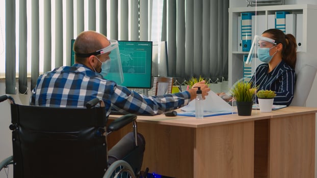 Paralysed financial worker in wheelchair with protection mask working in new normal business office talking with colleague. Immobilized freelancer in corporate company respecting social distance. photo