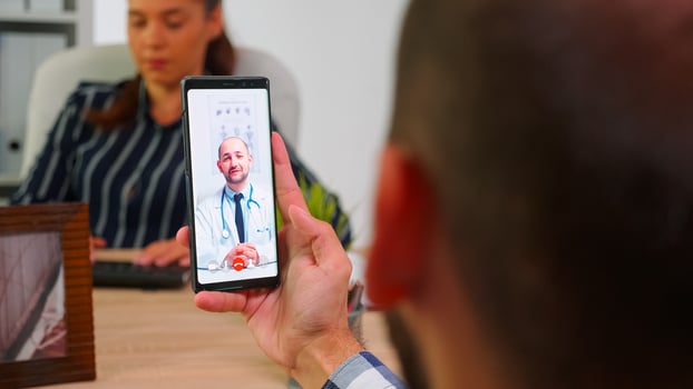 Disabled businessman talking on video call with doctor in work time sitting in wheelchair in modern company office using smartphone. Remotely medic advising freelancer using modern technology photo