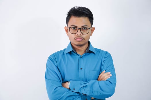 angry asian man with glasses standing with crossed arms and looking at camera wearing blue shirt isolated on white background photo
