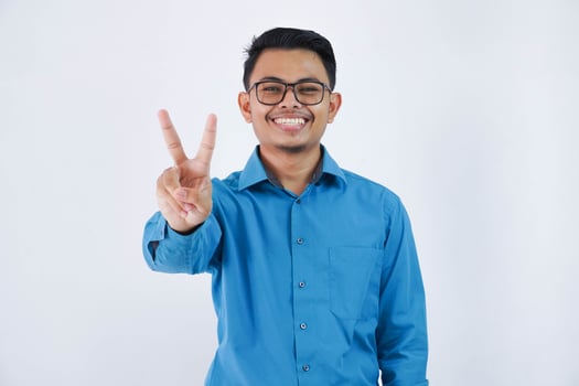 positive or happy asian man with glasses V-shaped finger gesture or peace wearing blue shirt isolated on white background photo
