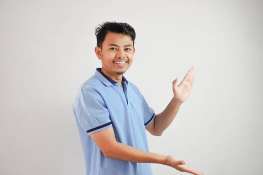 smiling asian man open arms pointing to the sides wearing blue t shirt isolated on white background photo
