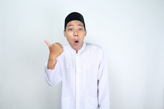 shocked asian man muslim show thumbs up and pointing to beside isolated on white background photo