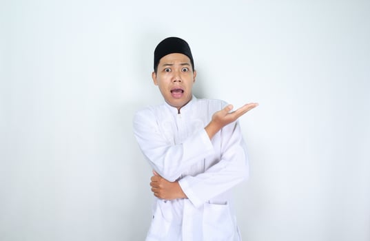 asian man muslim raising palm presenting to beside with shocked face expression isolated on white background photo
