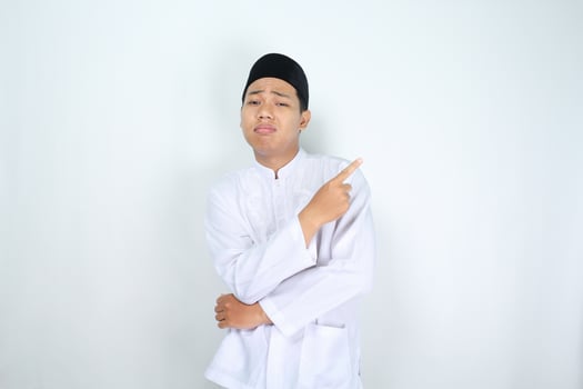 stressed muslim man asian pointing to empty side with folded hand isolated on white background photo