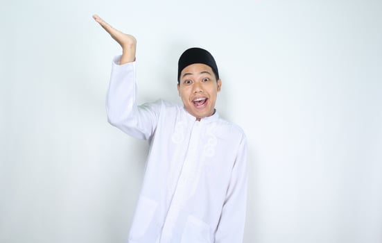funny asian muslim man with surprised expression raising hand to presenting isolated on white background photo