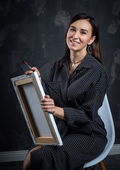 a young brunette female artist stands behind an easel. photo