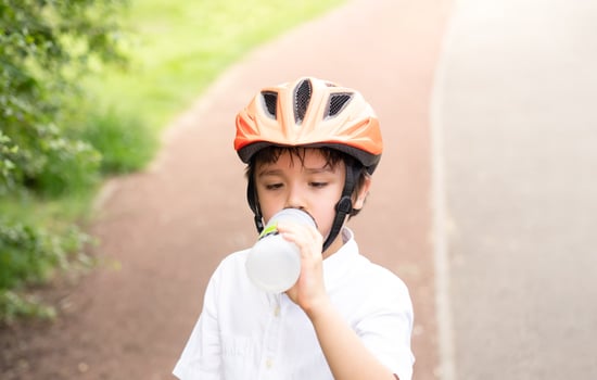 Healthy child boy wearing a bike helmet and drinking water,  kid Thirsty boy holding a bottle of water wearing a cycling helmet riding a bicycle in the park, Concept for safety, childhood health care photo