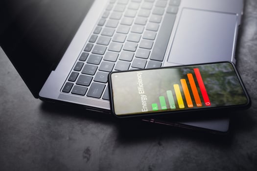 Smartphone resting on laptop with rate energy efficiency and eco home renovation interface on screen. Low consumption ecological house, sustainable development concept. photo