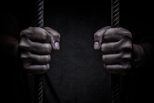 closeup on hands of man sitting in jail. Man behind jail bars on black background photo