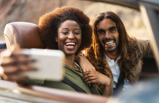 Happy young couple taking selfie with mobile smartphone while doing road trip - Travel people having fun driving in convertible car discovering new places - Relationship and vacation lifestyle concept photo