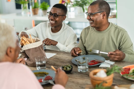 Happy afro Latin family eating healthy lunch with fresh vegetables at home - Food and parents unity concept photo