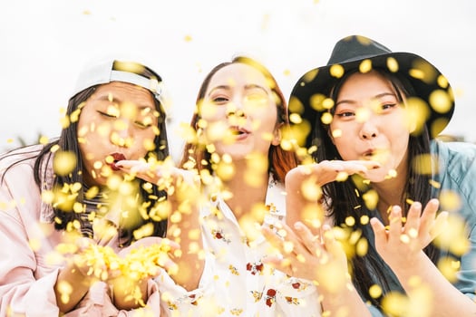 Happy Asian friends doing party throwing confetti outdoor - Young people having fun celebrating at festival event outside - Friendship, fest, entertainment and youth lifestyle concept photo