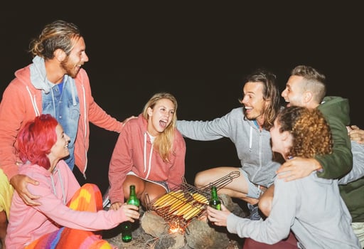Happy friends camping together and cooking corn at night outdoor - Young people having fun and laughing around bonfire - Friendship, party, lifestyle, wild concept photo