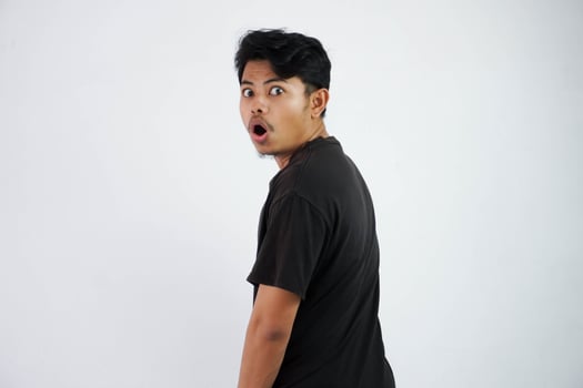 shocked Asian young man black t shirt open mouth feels amazed turn back to looking camera isolated on white background photo