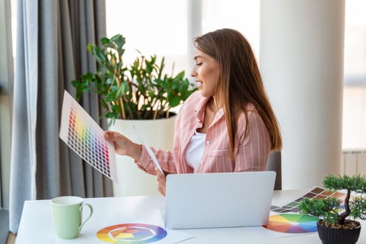 Cheerful youn woman designer having video conference with clients, sitting at desk in front of computer, holding color palettes, gesturing and smiling, copy space photo