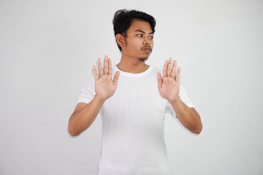 serious young Asian man showing stop gesture, demonstrating denial sign wearing white t shirt isolated on white background photo