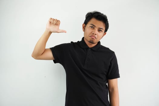 young asian man showing thumb down sign with negative expression wearing black polo t shirt isolated on white background photo