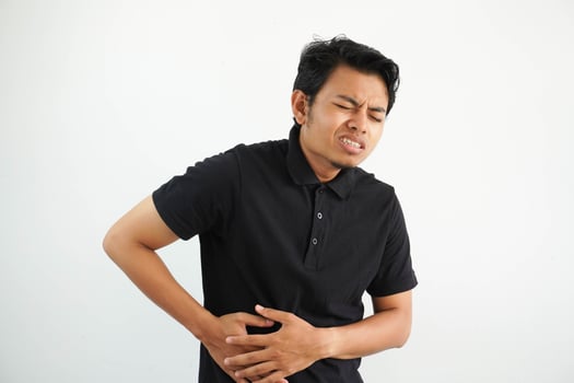 young asian man posing on a white backdrop wearing black polo t shirt hands holding stomach, having a liver pain, stomach ache. photo