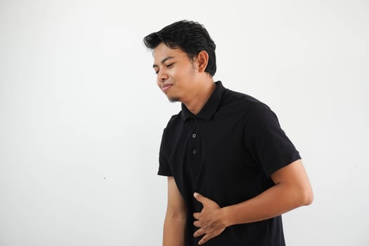 young asian man posing on a white backdrop wearing black polo t shirt touches tummy, smiles gently, eating and satisfaction concept. photo