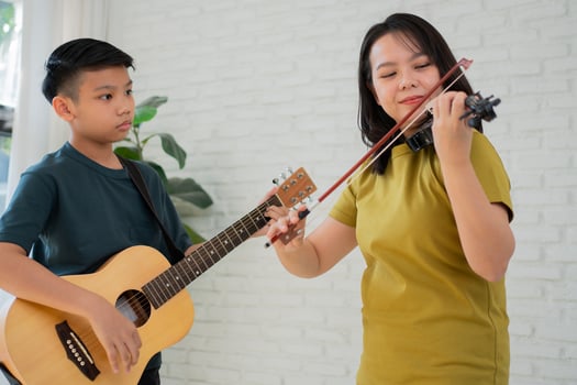 Asian boy playing guitar and mother playing violin, feel appreciated and encouraged. Concept of a happy family, learning and fun lifestyle, love family ties photo